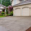 Large beige house with three car garage and large wet driveway with blue sky.